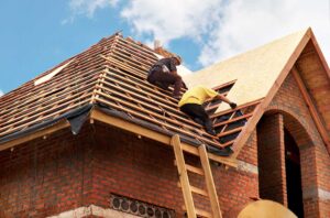 Roof valley with lifted shingles, exposed flashing, wet leaves, and water stains on the ceiling below